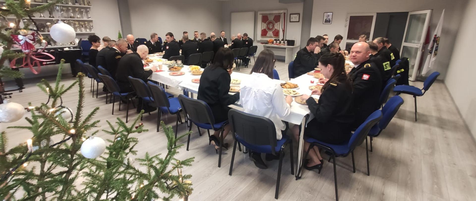 Funkcjonariusze KP PSP w Wolsztynie siedzą przy stole i jedzą wigilijne potrawy.