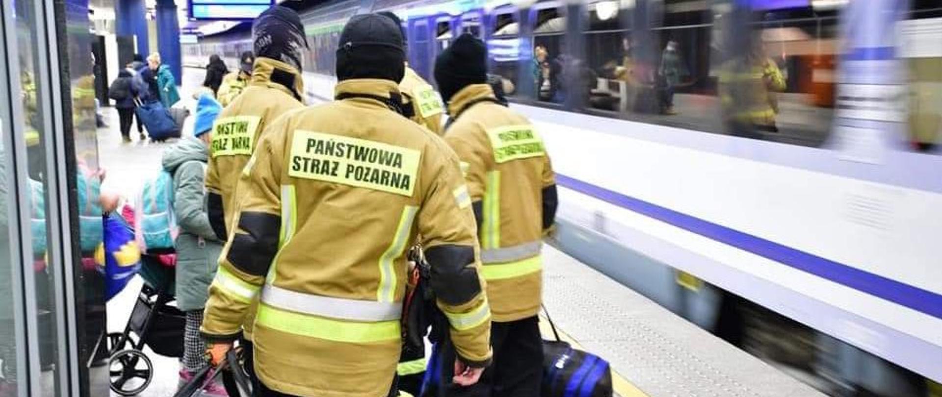 Zdjęcie przedstawia strażaków z bagażami pomagającym uchodźcom z Ukrainy.