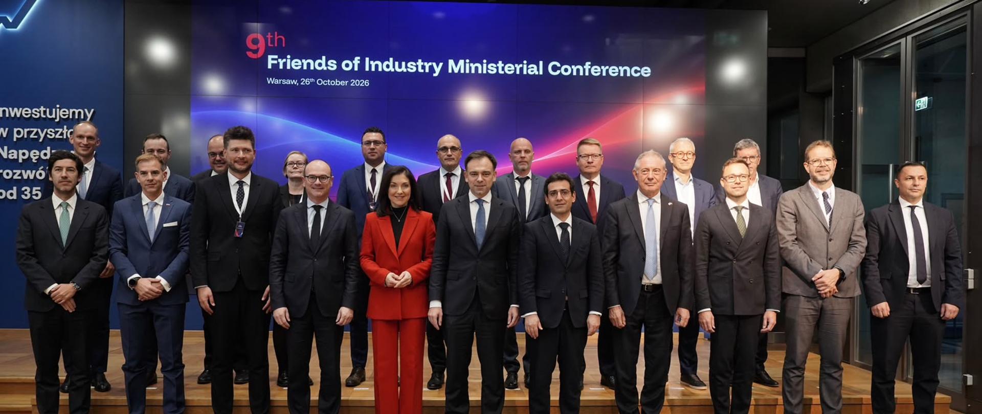 Friends of Industry - zdjęcie zbiorowe. Delegaci stoją w dwóch rzędach. Za nimi telebim z napisem 9th Friends of Industry Ministerial Conference