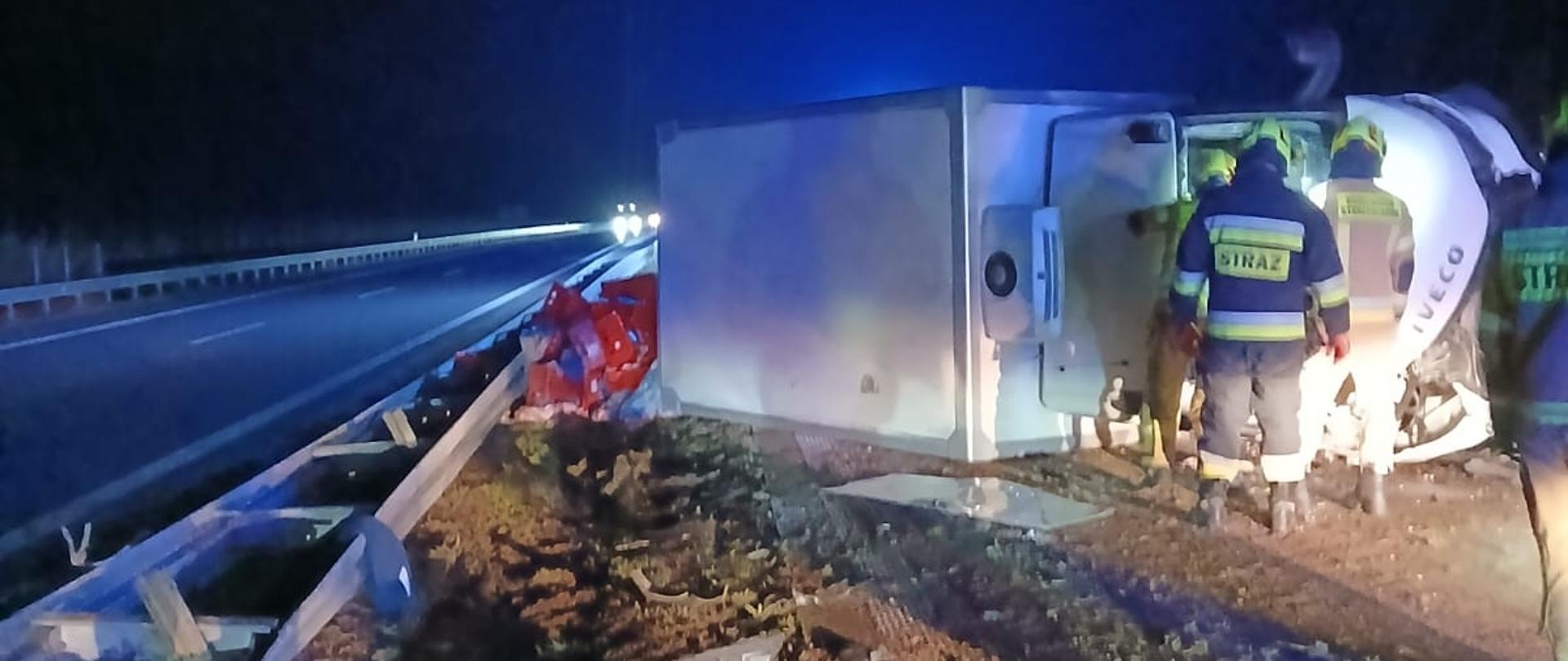 samochód dostawczy lezy na boku przy nim strażacy