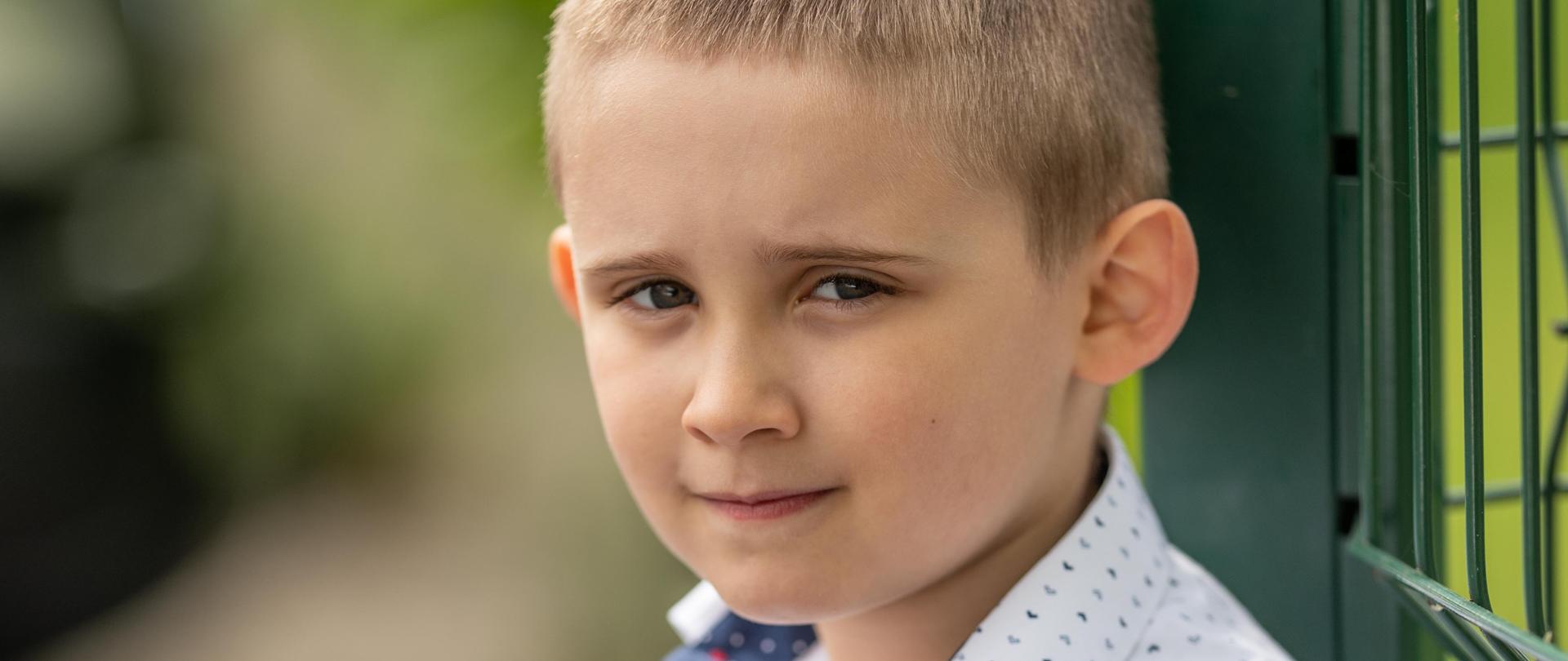 Zdjęcia chłopca opartego o metalowy płot.