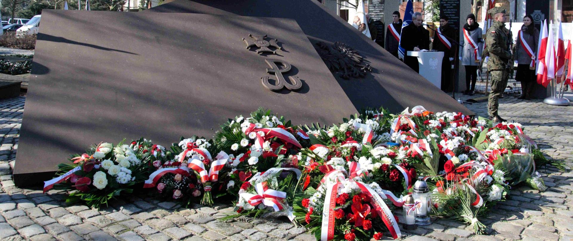 duą betonowa płyta pomnik przed którym leżą niało czerwone wiążanki