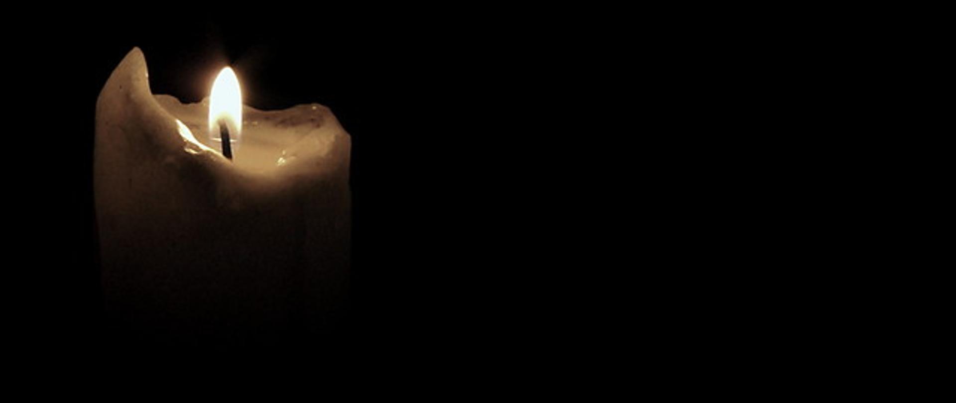 Zdjęcie przedstawia płonącą świecę na ciemnym tle. 