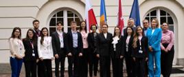 Grupa ludzi stoi przed budynkiem pozując do zdjęcia, z tyłu widać flagę m.in. Polski i Mołdawii