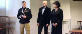 Zastępca Komendanta CS PSP przemawia na otwarciu odprawy, po jego lewej stronie stoi mężczyzna oraz kobieta