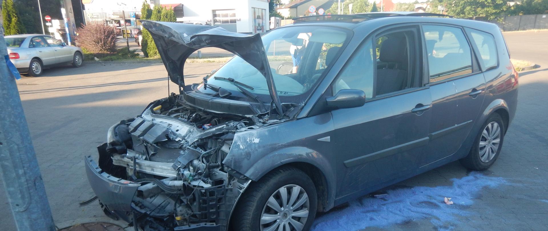 Zdjęcie przedstawia samochód, który brał udział w zdarzeniu. Samochód ma uszkodzony przód. Dookoła znajduje się rozsypany sorbent.