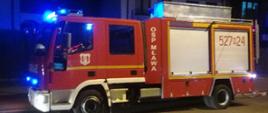 Wóz strażacki z OSP Mława zaparkowany na ulicy. Na drugim planie widać blok mieszkalny