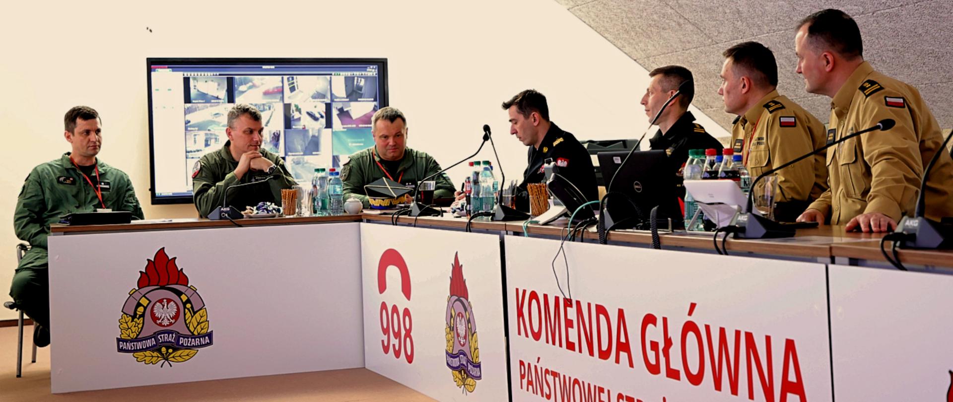 Przedstawiciele PSP i RSZ RP siedzą przy stole podczas spotkania. Na froncie stołów widnieje napis Komenda Główna Państwowej Straży Pożarnej, 998 i logo PSP