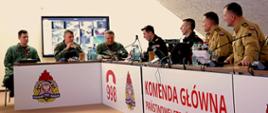 Przedstawiciele PSP i RSZ RP siedzą przy stole podczas spotkania. Na froncie stołów widnieje napis Komenda Główna Państwowej Straży Pożarnej, 998 i logo PSP