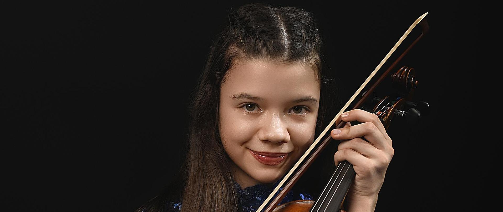 Zdjęcie przedstawiające Emilię Kalinowską ze skrzypcami podczas sesji zdjęciowej. Emilia ubrana jest w niebieską suknię.