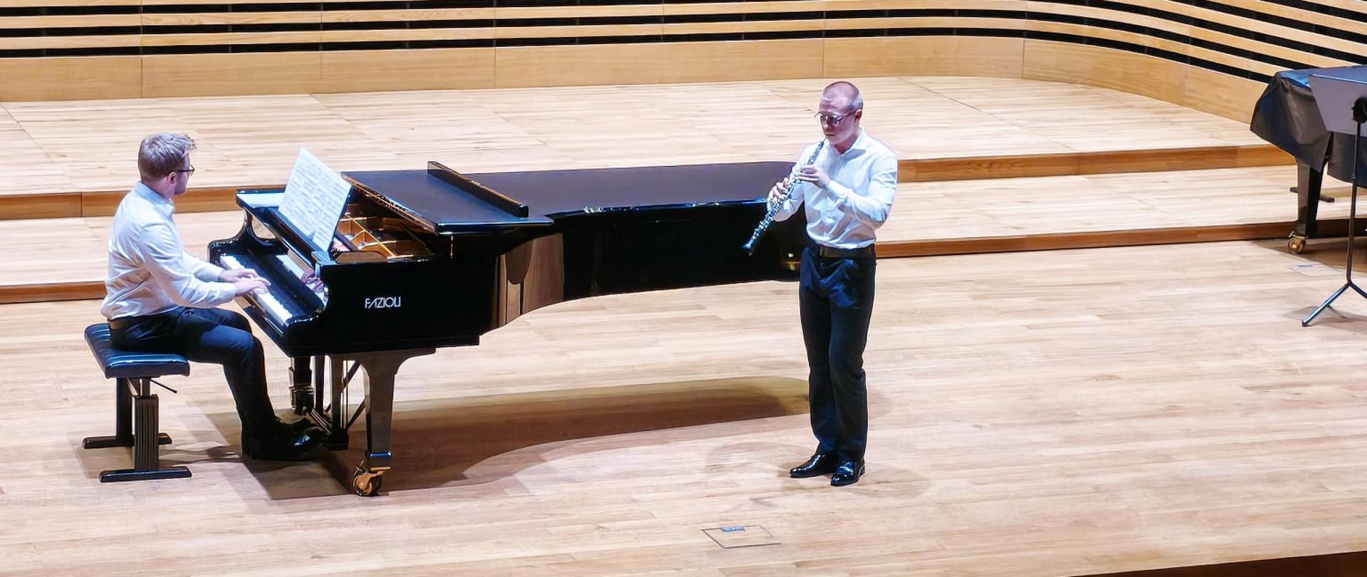 Chłopak gra na oboju, mężczyzna akompaniuje na fortepianie.