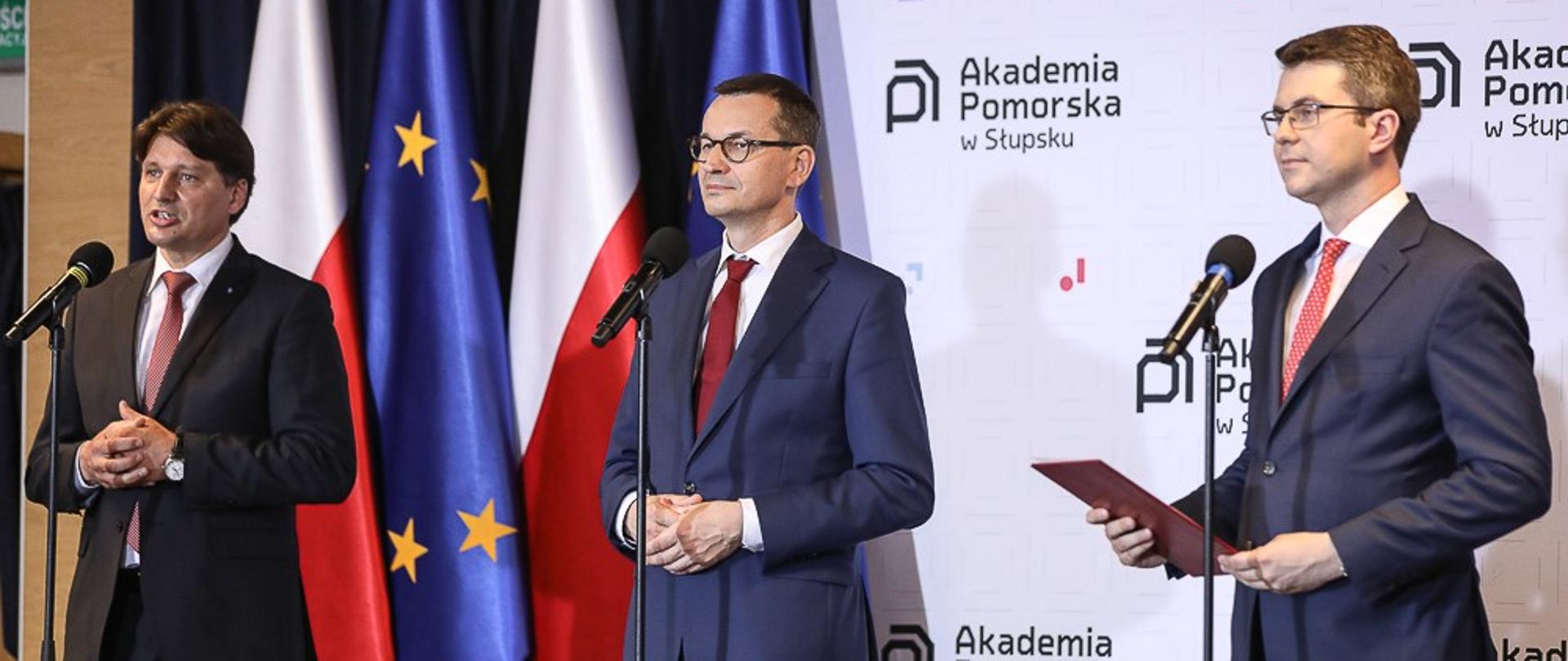 Premier Mateusz Morawiecki i minister Piotr Muller stoją podczas konferencji prasowej.