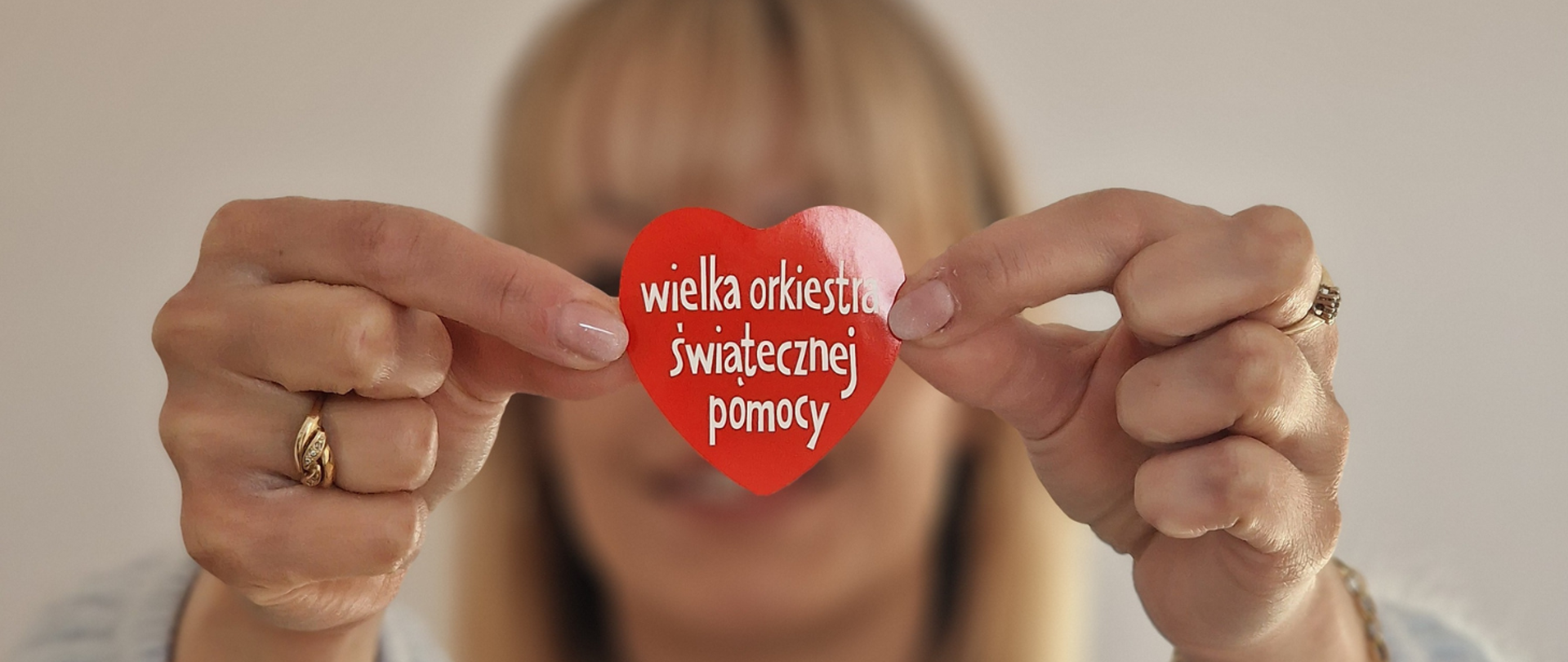 Dłonie trzymające czerwone serduszko Wielkiej Orkiestry Świątecznej Pomocy z widocznym napisem „wielka orkiestra świątecznej pomocy”.