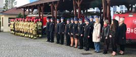 Funkcjonariusze, pracownicy cywilni Komendy Wojewódzkiej Państwowej Straży Pożarnej stoją na baczność podczas uroczystości. Za nimi stoją zabytkowe pojazdy Państwowej Straży Pożarnej.