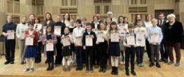 Na scenie stoi duża grupa uczestników konkursu - uczniów i nauczycieli. Uczniowie trzymają w dłoniach dyplomy.