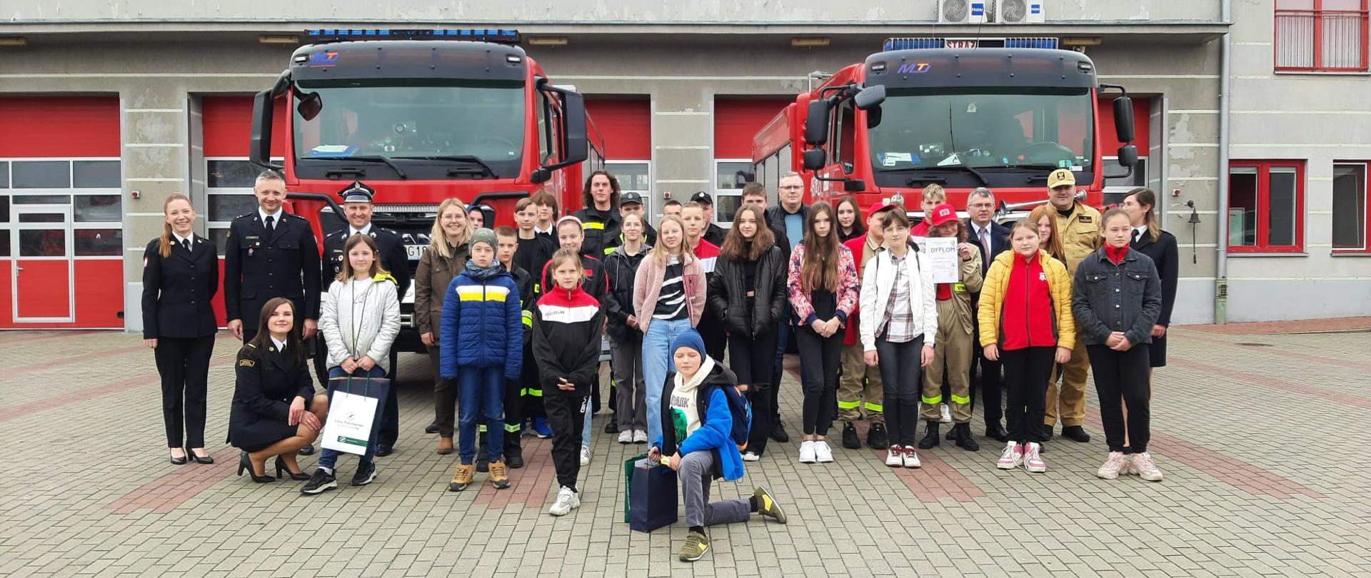 Uczestnicy eliminacji powiatowych OTWP wraz z przedstawicielami na tle samochodów pożarniczych.