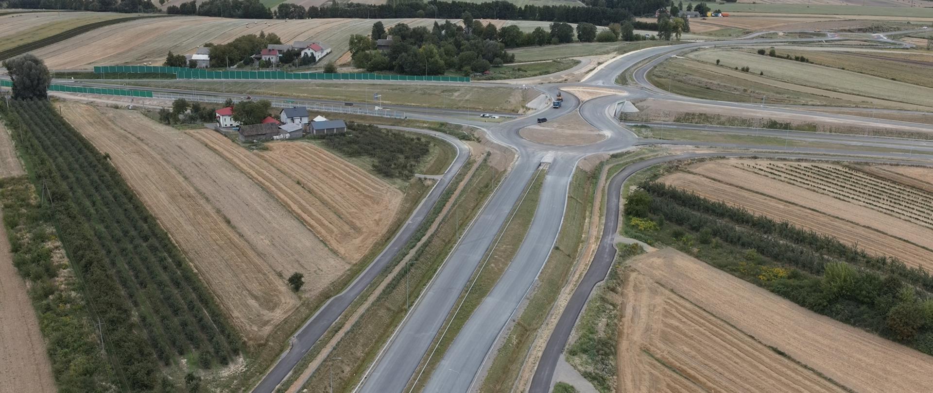 Budowa obwodnicy Opatowa - zdjęcie dwujezdniowej drogi wykonane z drona, w oddali podłużne rondo
