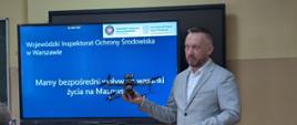Inspektor Wojewódzkiego Inspektoratu Ochrony Środowiska w Warszawie Delegatura w Ciechanowie prezentuje drona w klasie; na ekranie za nim widać slajd o ochronie środowiska.