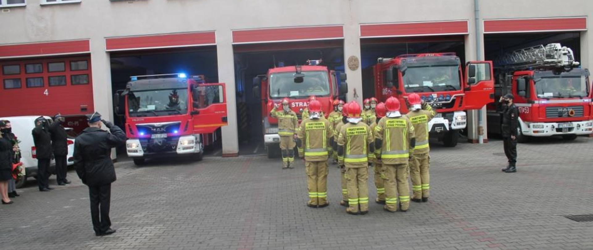 Zdjęcie przedstawia funkcjonariuszy PSP oraz samochody ratowniczo-gaśnicze podczas uroczystej zmiany służby