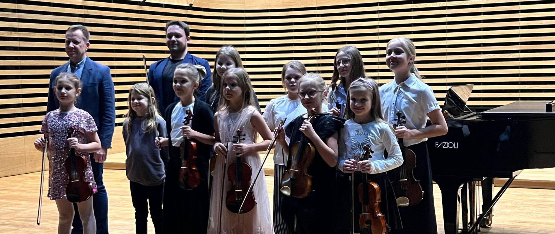 Wszyscy wykonawcy stoją z nauczycielem i akompaniatorem na estradzie.