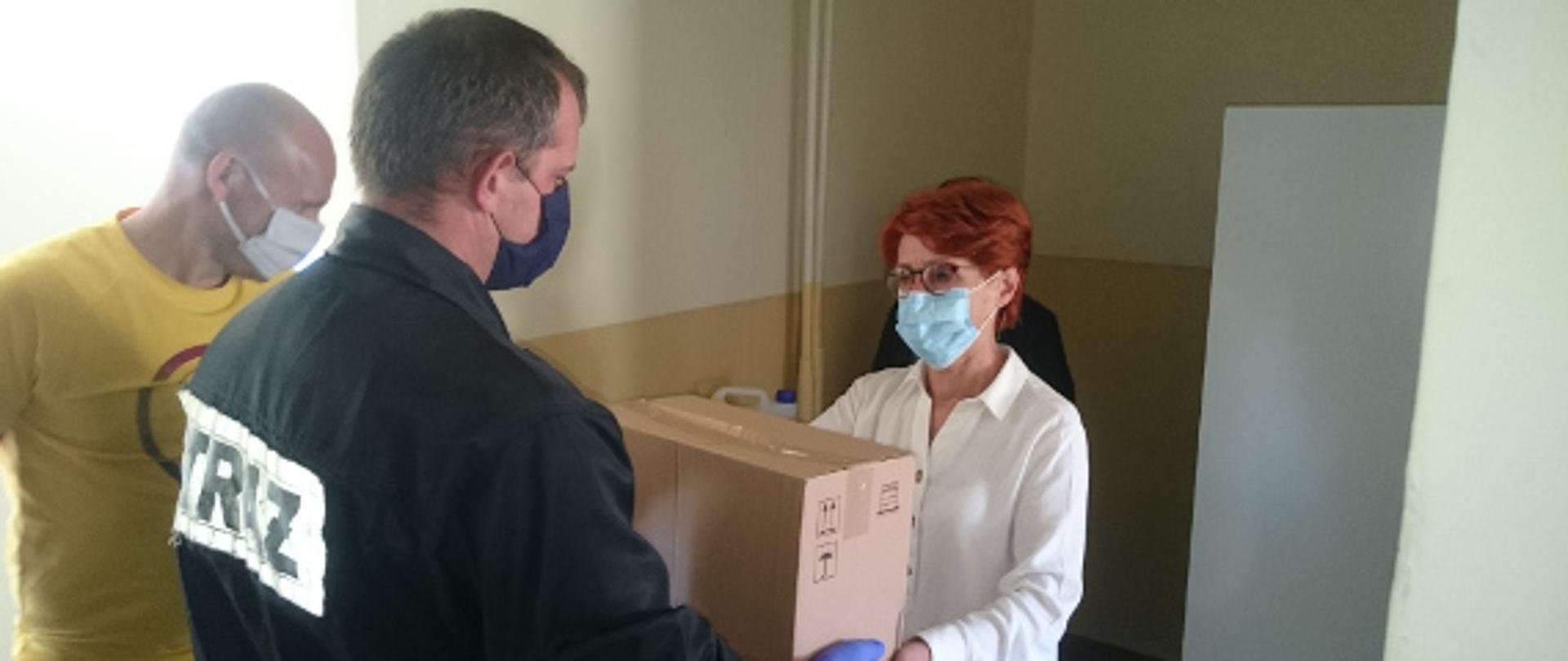 Pani dyrektor odbiera pudło ze środkami wręczane przez strażaka psp. 