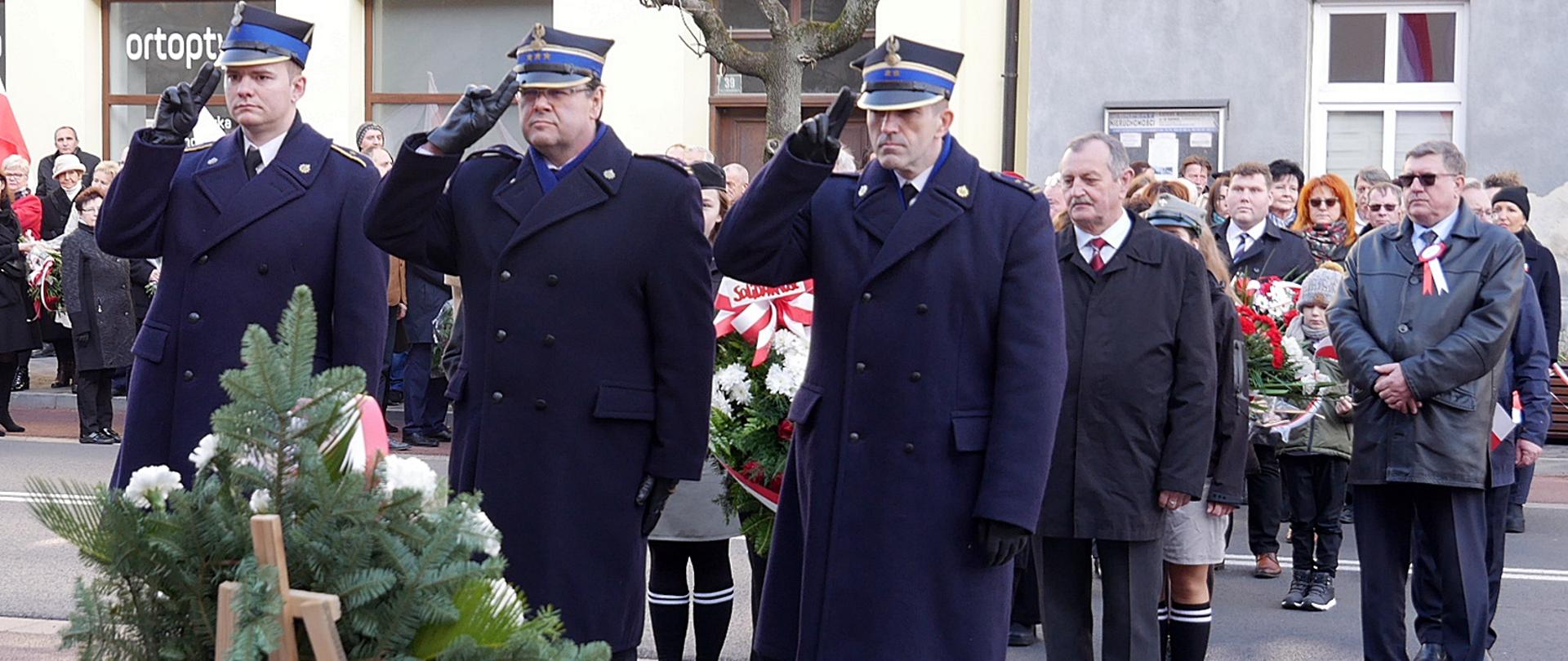 Widok z przodu. Delegacja strażaków KP PSP w Wadowicach salutuje po złożeniu wiązanki pod pomnikiem żołnierzy 12 Pułku Piechoty Wojska Polskiego. W tle pozostałe delegacje