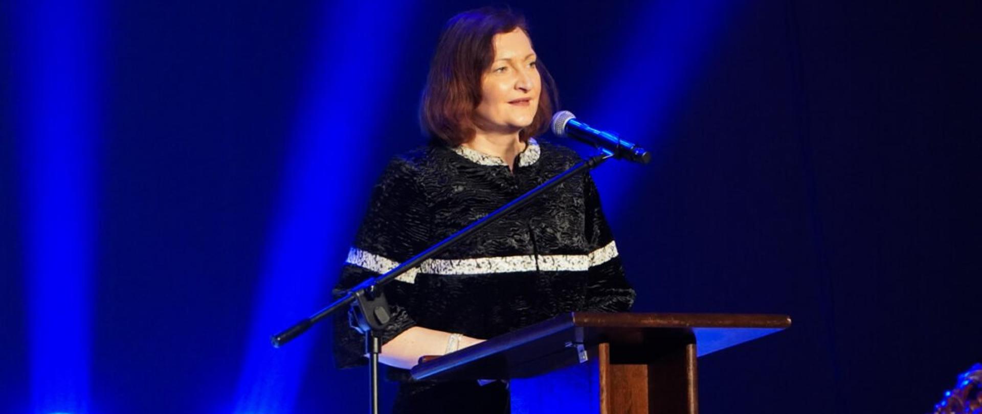 Wojewoda podkarpacki Ewa Leniart przemawia podczas uroczystości 668. rocznicy lokacji Rzeszowa. Stoi przy mównicy, oświetla ją niebieskie światło z reflektorów.