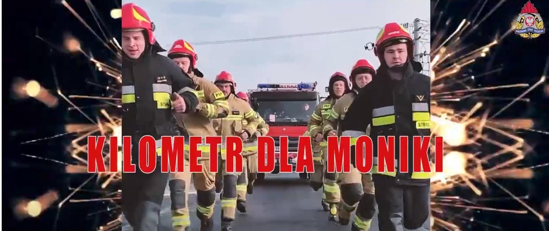 W środkowej części zdjęcia widzimy biegnących strażaków w ubraniach specjalnych i hełmach. Za nimi widoczny częściowo samochód ratowniczo – gaśniczy. Z prawej i lewej strony zdjęcia widoczne iskry oraz w prawym górnym rogu znak PSP.