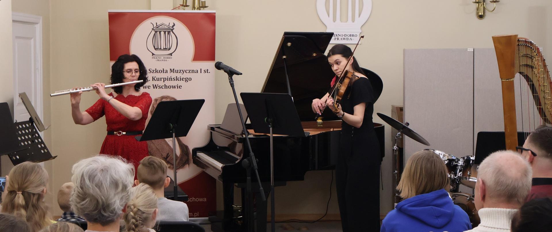 Flecistka i skrzypaczka wykonujące utwór muzyczny przed publicznością.