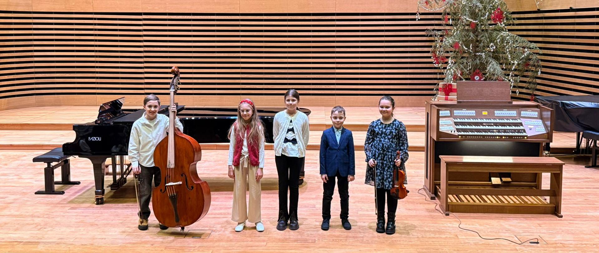 Dwóch chłopców i trzy dziewczynki stoją na scenie ze swoimi instrumentami.