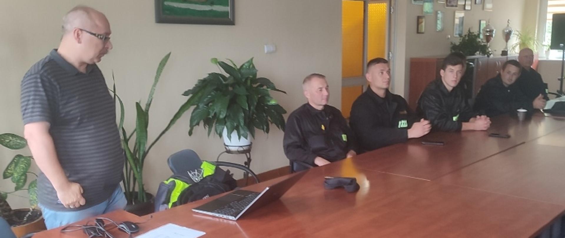 Sala szkoleniowa Okręgowej Spółdzielni Mleczarskiej we Włoszczowie, przy stole na którym ustawiony jest laptop stoi prowadzący szkolenie, przedstawiciel firmy dostawcy instalacji regazyfikacji, na drugim planie przy stole siedzą strażacy, uczestnicy szkolenia