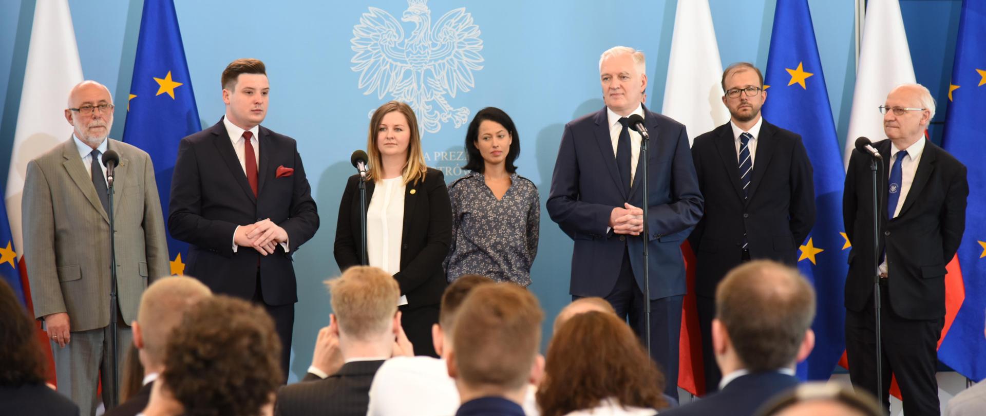 Przedstawiciele kierownictwa MNiSW na tle niebieskiej ściany z godłem RP