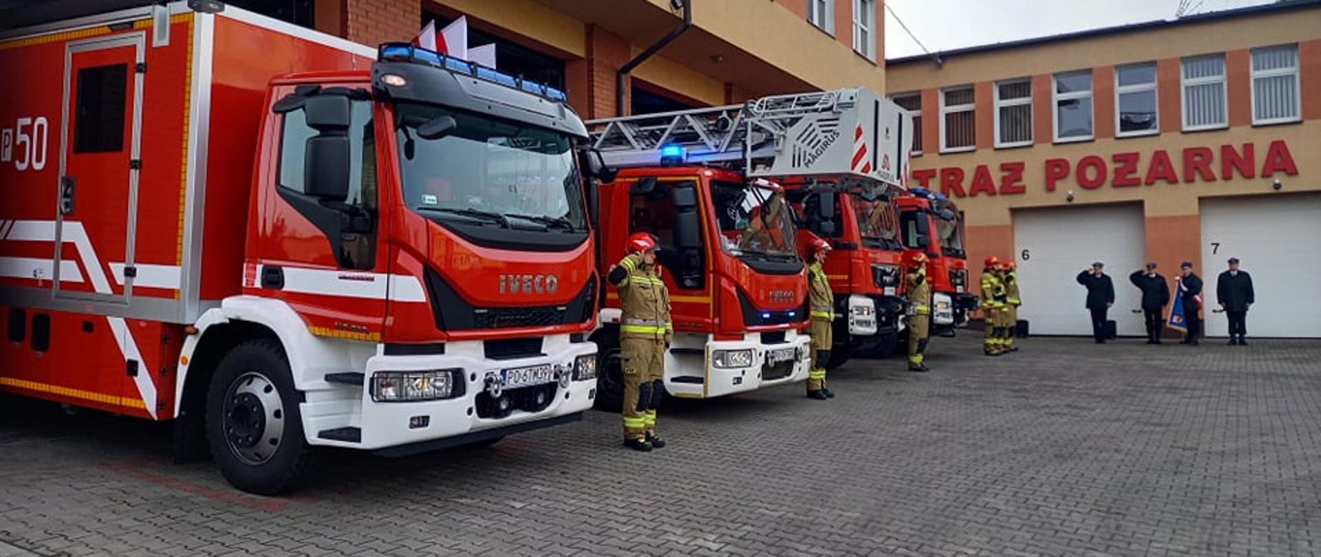Zdjęcie przedstawia strażaków odśpiewujących Mazurka Dąbrowskiego na palcu Komendy oraz samochody strażackie.
W tle budynek Komendy.
