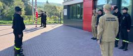 Zdjęcie przedstawia poczet flagowy oraz strażaków podczas uroczystej zmiany służby wraz z podniesienie flagi państwowej na maszt