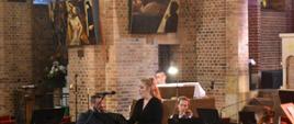 na zdjęciu, w kościele OO. Franciszkanów, podczas koncertu w ramach festiwalu Musica Classica w Jaśle widnieje solistka sopranistka i towarzyszący jej zespół kameralny (organy, dwoje skrzypce i wiolonczela) oraz zgromadzeni słuchacze. Kolorystyka zdjęcia jest biało-beżowo-brązowo-czarna. 