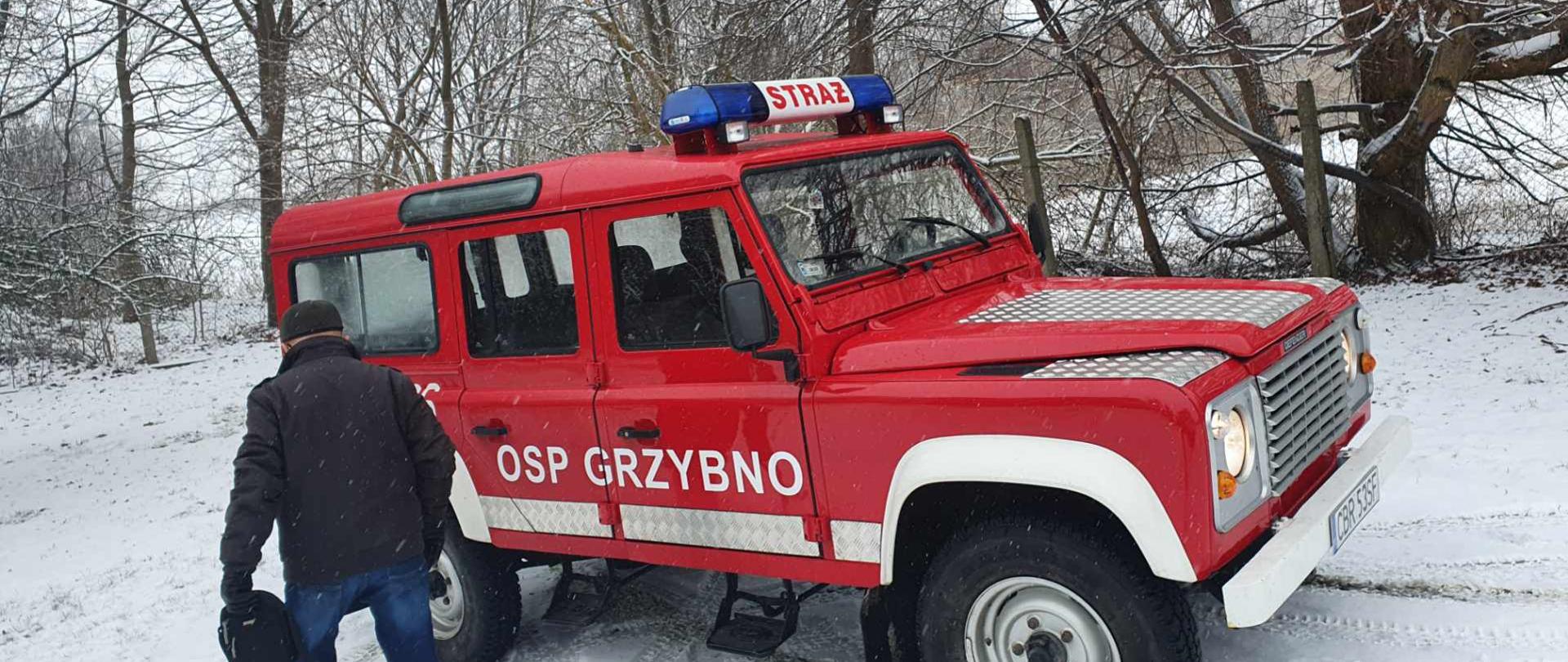 Zdjęcie przedstawia mężczyznę zmierzającego do samochodu OSP Grzybno w drodze do punktu szczepień. W tle sceneria zimowa.
