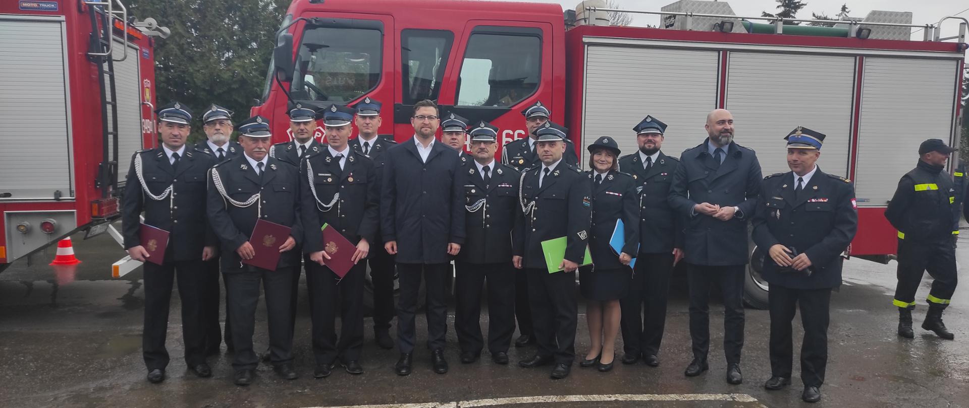 Na zdjęciu na tle samochodu strażackiego grupa strażaków w mundurach galowych oraz przedstawiciel rządu i samorządu.