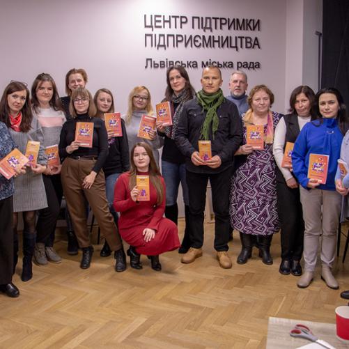 Grupa ludzi pozuje do zdjęcia z ulotkami i podręcznikami w jednakowych kolorach.