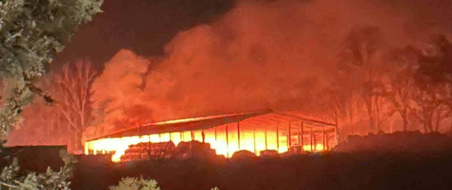 Duży ogień pod wiatą, nad nią dużo dymu, jest ciemno