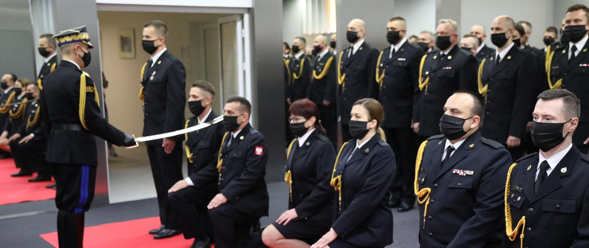 Komendant Główny PSP nadbrygadier Andrzej Bartkowiak i Zastępca Komendanta Głównego nadbrygadier Adam Konieczny w trakcie pasowania na oficera i wręczania aktu nadania pierwszego stopienia oficerskiego funkcjonariuszom PSP. W tle awansowani funkcjonariusze. 