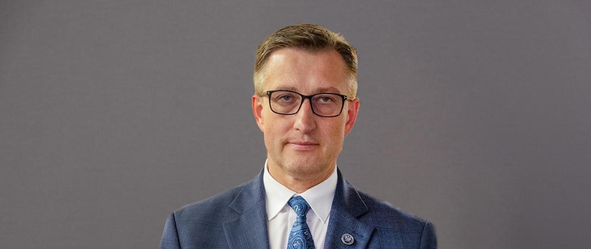 Dyrektor generalny Marcin Iskra na tle szarej ściany.