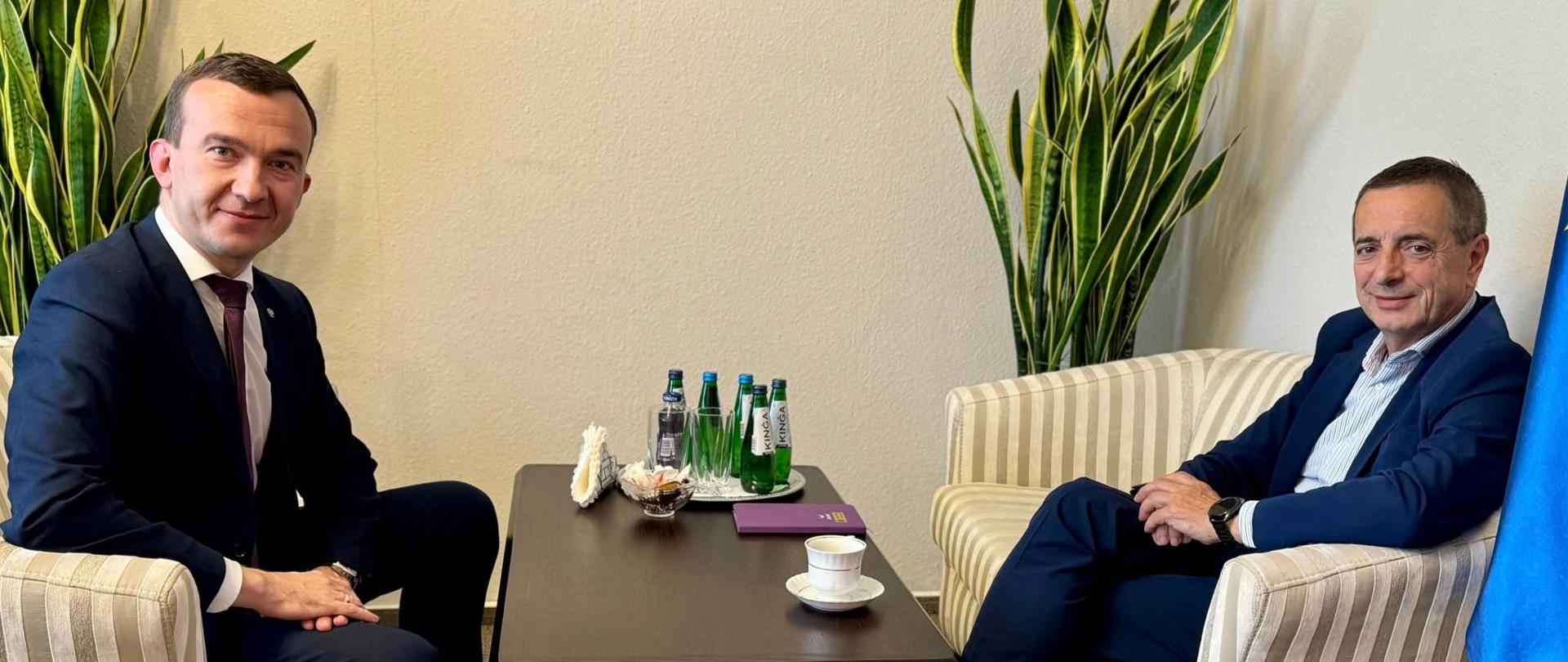 Dwóch mężczyzn w garniturach siedzi przy stoliku 