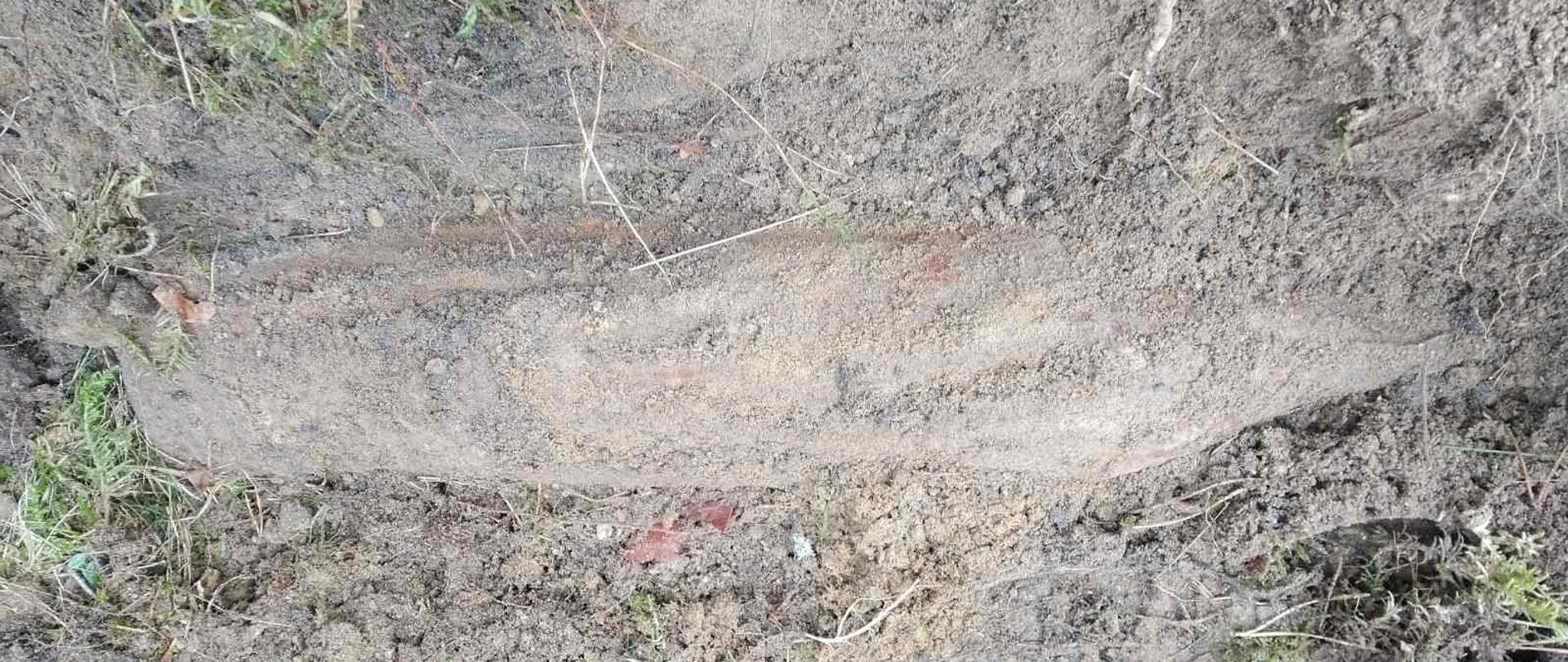 Częściowo okopany niewybuch leżący w ziemi.