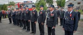 Na zdjęciu druhowie OSP odznaczeni. Strażacy w mundurach galowych koloru granatowego. W tle samochód pożarniczy i zaproszeni na uroczystość przekazania samochodu ratowniczo-gaśniczego dla OSP Smerekowiec goście 