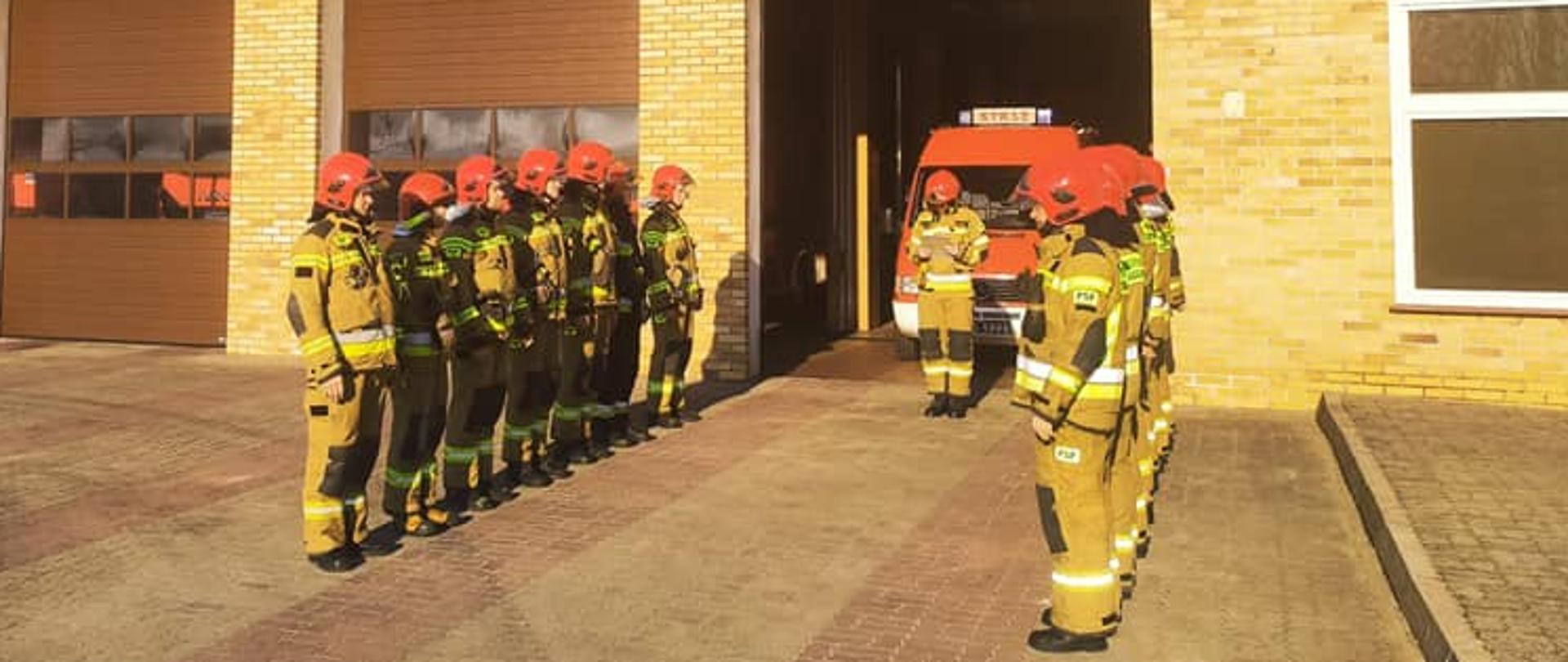 Strażacy stojący w dwóch rzędach przed otwarta brama wyjazdową