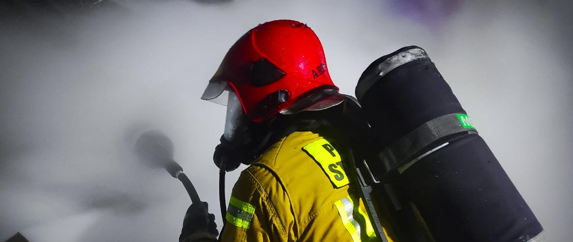 Na zdjęciu znajduję się strażak gaszący palące się drewno