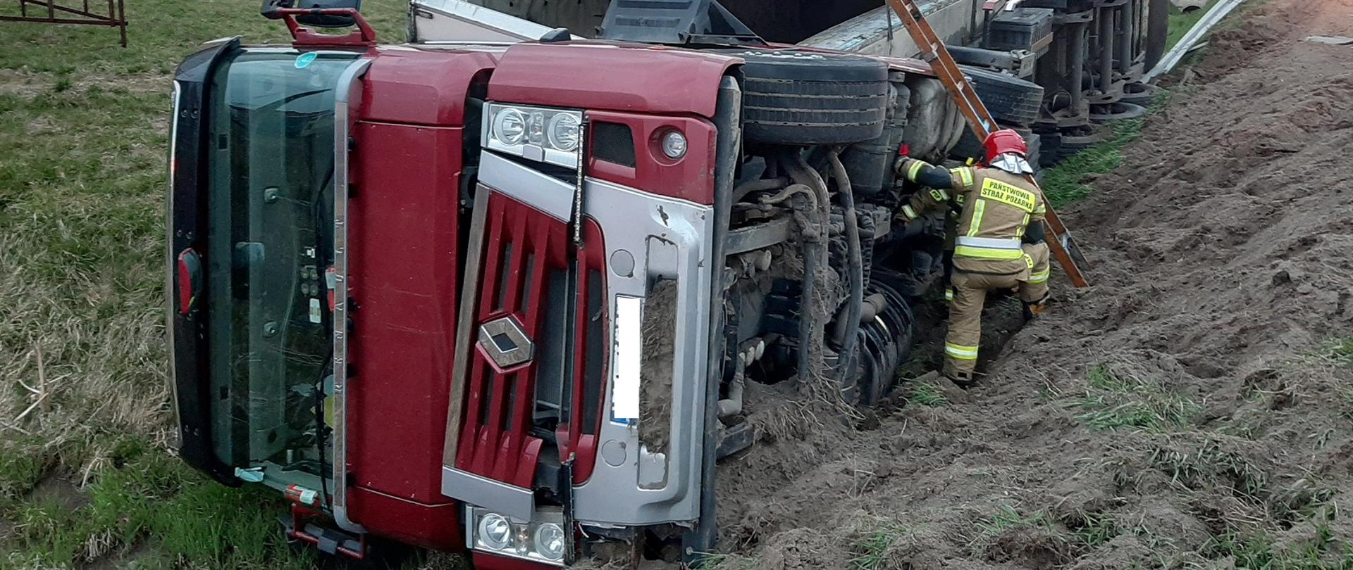 Przewrócony samochód ciężarowy w rowie. Obok stoją ratownicy PSP.