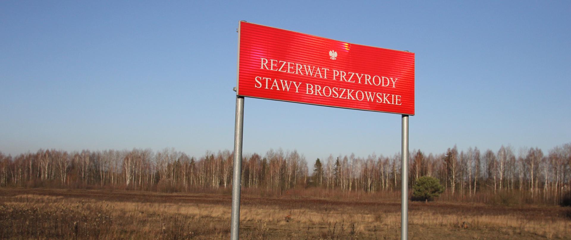 Czerwona tablica urzędowa z napisem "Rezerwat przyrody Stawy Broszkowskie"