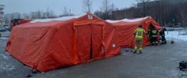 Na zdjęciu czerwone namioty w których przeprowadzane są testy na obecność covid-19, przed namiotami strażacy w ubraniach z napisem Państwowa Straż Pożarna oraz Straż