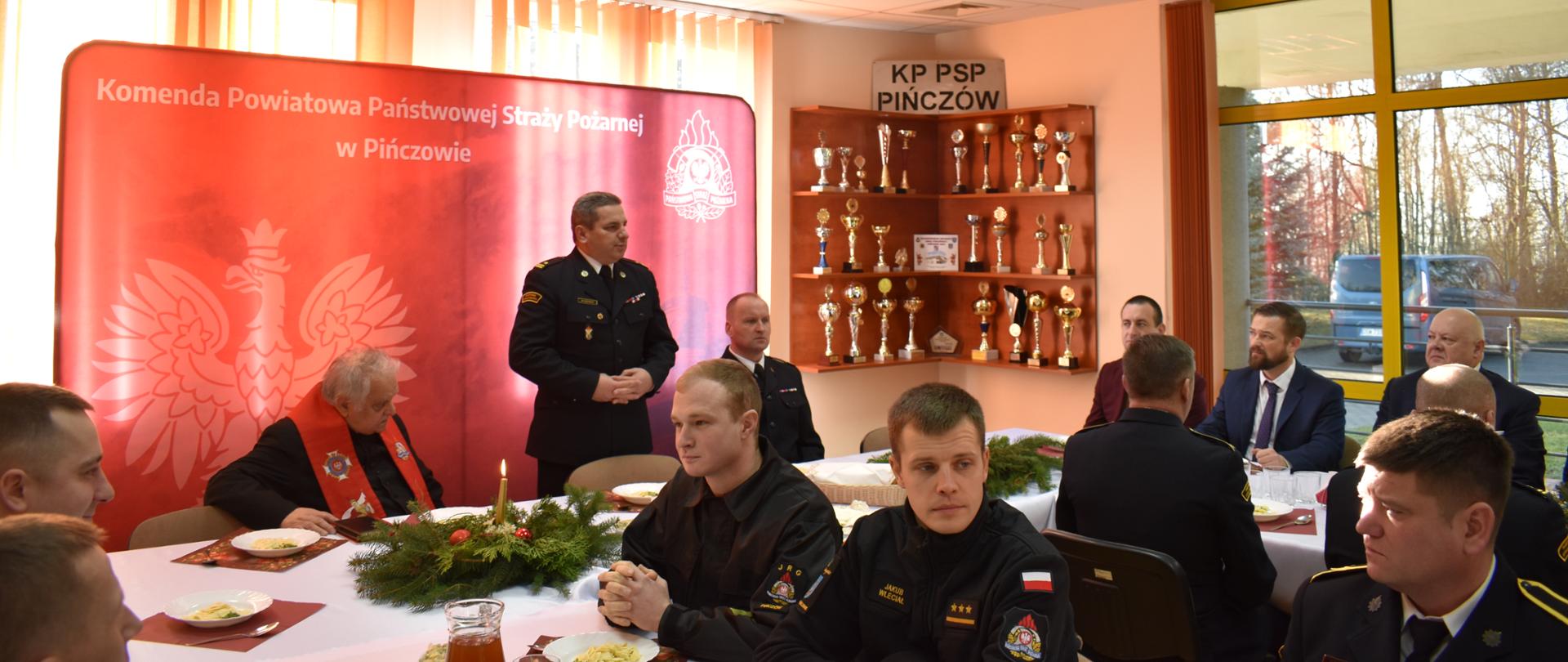 Zdjęcie przedstawia Komendanta Powiatowego składającego świąteczne życzenia osobą obecnym na świątecznym spotkaniu.